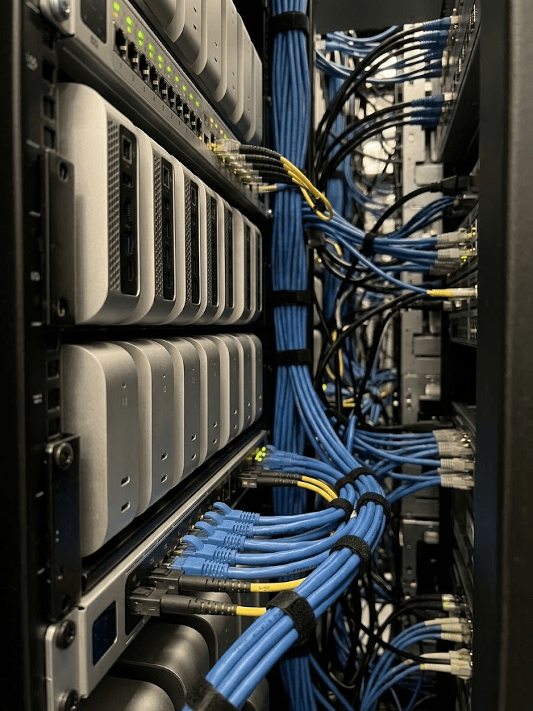 Close-up of Mac minis in a rack next to a network switch and bundled cables