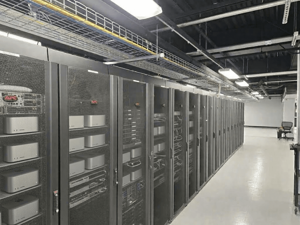 A long aisle of black server cabinets holding Mac computers